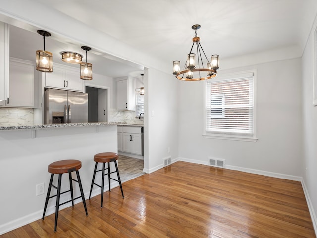 kitchen featuring white cabinetry, hardwood / wood-style flooring, light stone countertops, and stainless steel refrigerator with ice dispenser