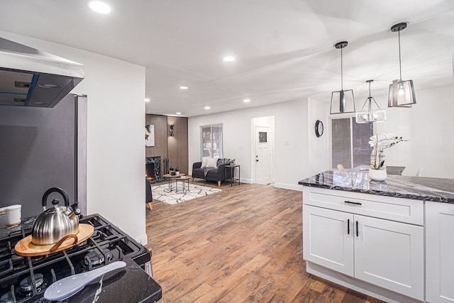 kitchen with white cabinetry, dark stone countertops, gas range oven, dark hardwood / wood-style flooring, and decorative light fixtures