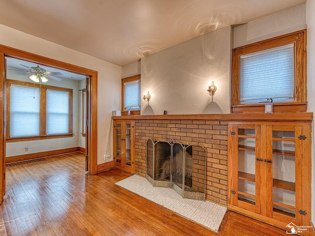 unfurnished living room with hardwood / wood-style flooring, ceiling fan, and a brick fireplace