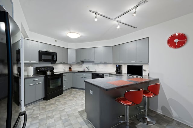 kitchen featuring black appliances, gray cabinets, a sink, dark countertops, and a peninsula