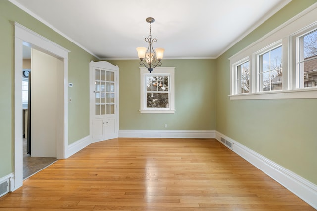 unfurnished dining area featuring an inviting chandelier, ornamental molding, and light wood-type flooring