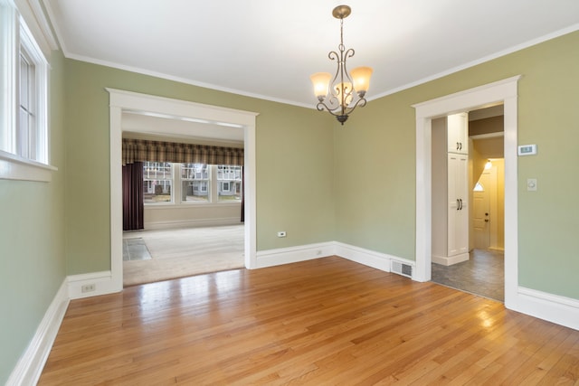 empty room with crown molding, an inviting chandelier, and light hardwood / wood-style flooring