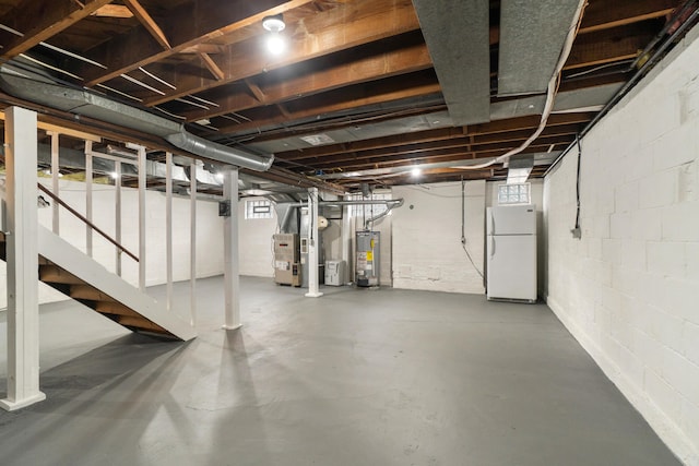 basement featuring heating unit, gas water heater, and white refrigerator