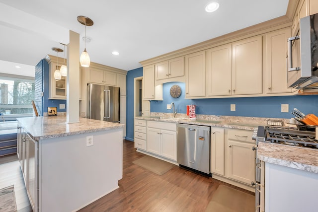 kitchen featuring pendant lighting, sink, hardwood / wood-style flooring, stainless steel appliances, and cream cabinets