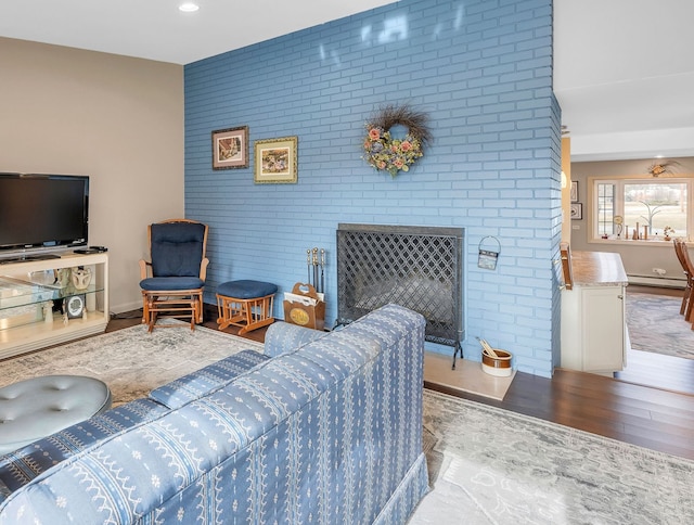 living room featuring brick wall, wood-type flooring, a fireplace, and a baseboard heating unit