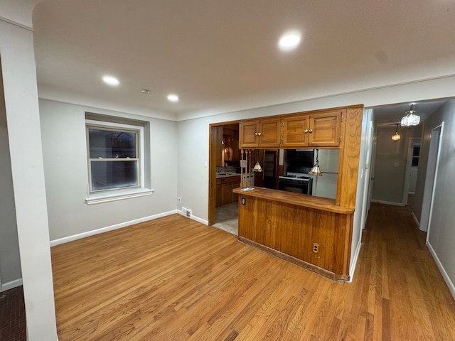 kitchen featuring pendant lighting, fridge, white range with gas cooktop, kitchen peninsula, and light wood-type flooring