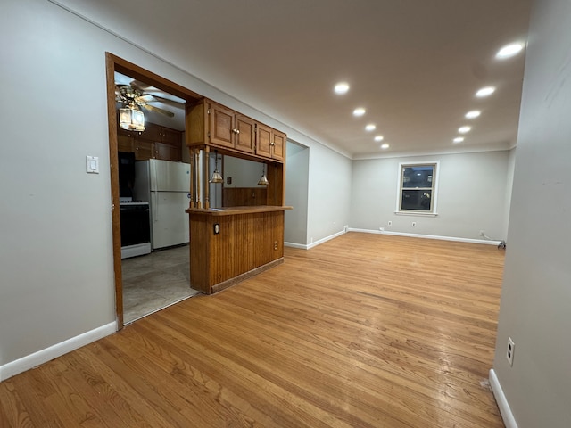 kitchen with a breakfast bar area, white appliances, light hardwood / wood-style flooring, kitchen peninsula, and ceiling fan