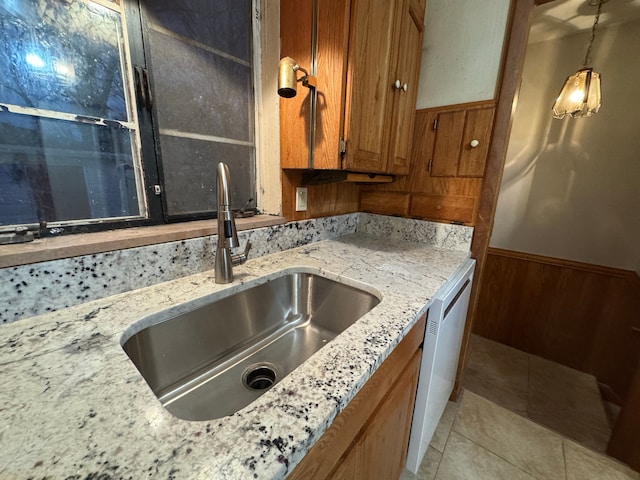 kitchen featuring pendant lighting, sink, stainless steel dishwasher, light tile patterned floors, and light stone countertops