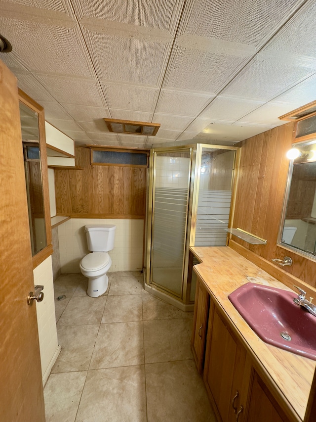 bathroom featuring vanity, a shower with shower door, tile patterned floors, and wooden walls