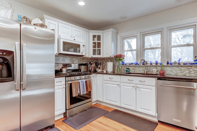 kitchen with sink, light wood-type flooring, appliances with stainless steel finishes, white cabinets, and backsplash