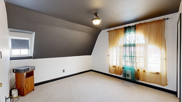 additional living space with lofted ceiling, a textured ceiling, light colored carpet, and a healthy amount of sunlight