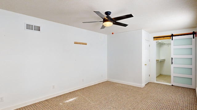 unfurnished bedroom with a spacious closet, light carpet, a closet, ceiling fan, and a barn door