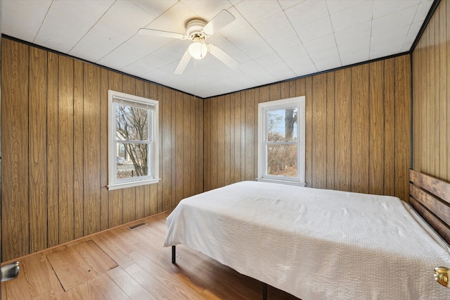 bedroom featuring multiple windows, hardwood / wood-style floors, wooden walls, and ceiling fan