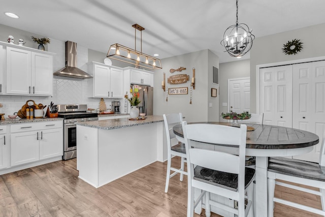 kitchen with appliances with stainless steel finishes, pendant lighting, wall chimney range hood, and white cabinets