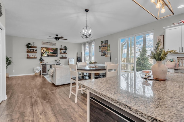 kitchen featuring wood-type flooring, pendant lighting, white cabinets, and light stone counters