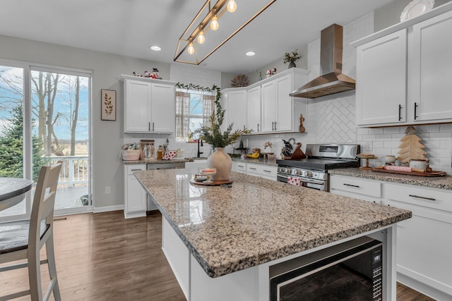 kitchen with wall chimney range hood, a center island, stainless steel range, white cabinets, and decorative light fixtures