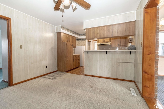 kitchen with a breakfast bar, light carpet, kitchen peninsula, white fridge, and ceiling fan