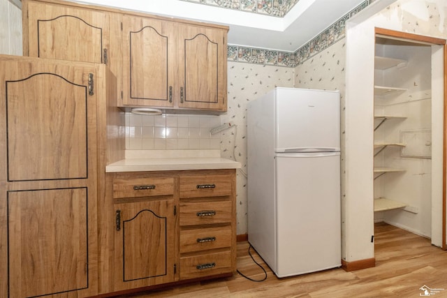 kitchen with white refrigerator, decorative backsplash, a skylight, and light hardwood / wood-style flooring