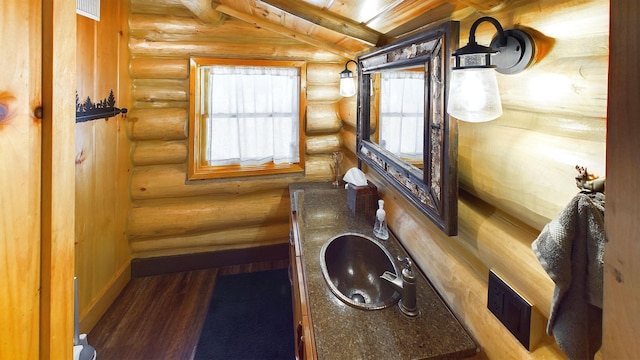 bathroom featuring visible vents, a sink, wood finished floors, baseboards, and vaulted ceiling with beams