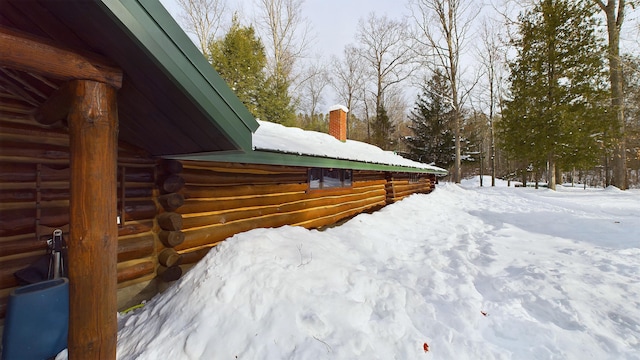 snow covered property with log exterior and a chimney