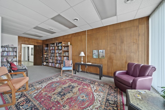 sitting room with carpet flooring, a drop ceiling, and wood walls