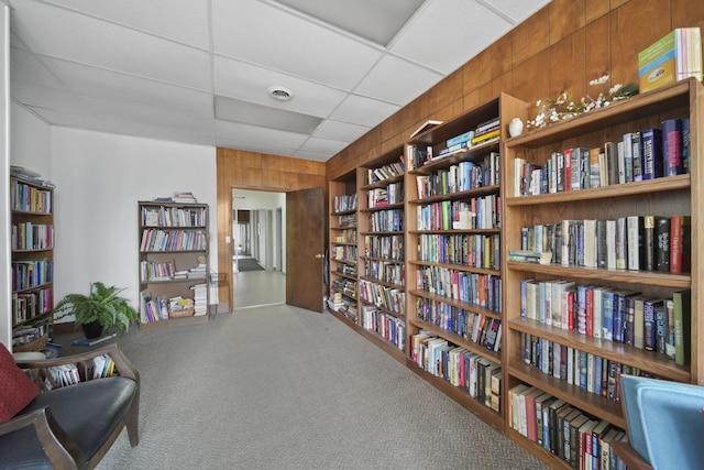 sitting room featuring carpet, a drop ceiling, built in features, and wood walls