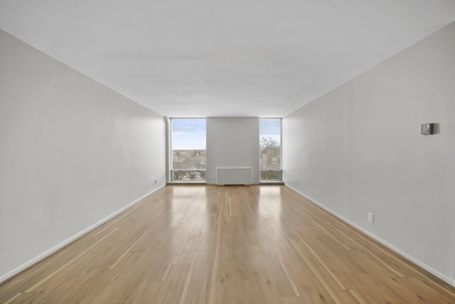 unfurnished room with expansive windows, radiator, and light hardwood / wood-style floors