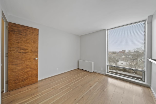 unfurnished room with expansive windows, radiator heating unit, and light hardwood / wood-style floors