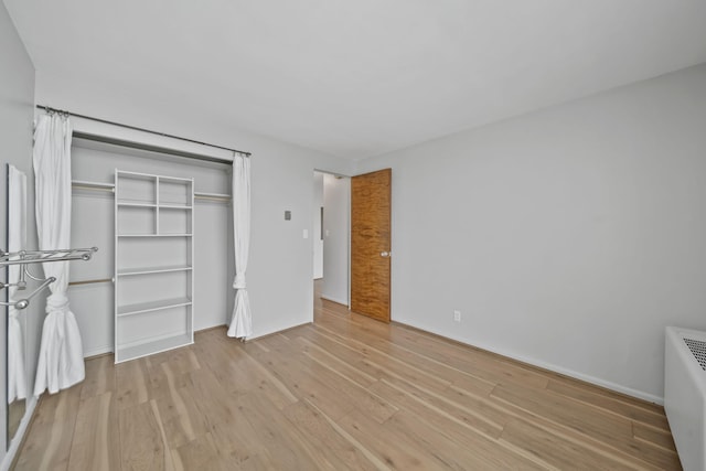 unfurnished bedroom featuring radiator heating unit, a closet, and light wood-type flooring