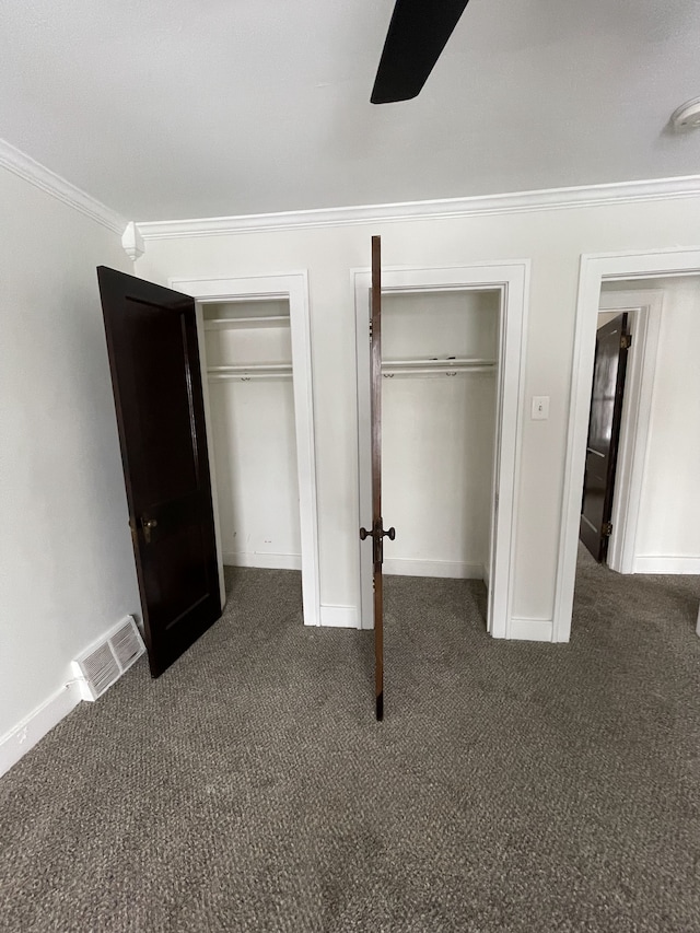 unfurnished bedroom featuring dark colored carpet, ceiling fan, ornamental molding, and two closets