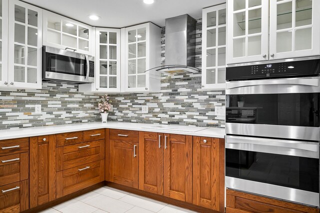 kitchen with tasteful backsplash, light tile patterned flooring, appliances with stainless steel finishes, and wall chimney range hood