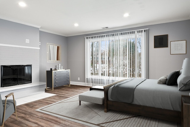 bedroom with hardwood / wood-style flooring, crown molding, and a brick fireplace