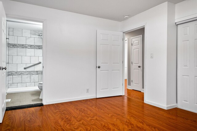 unfurnished bedroom with ensuite bath, wood-type flooring, and a closet