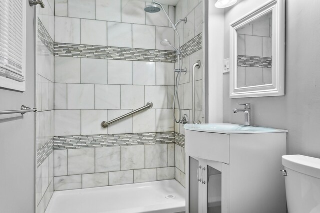 bathroom featuring a tile shower, vanity, and toilet