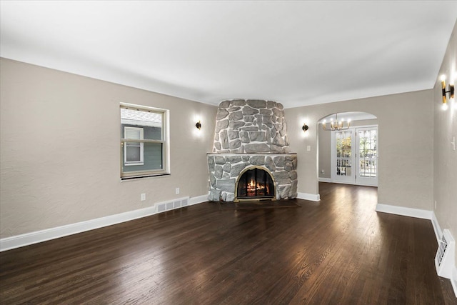 unfurnished living room featuring a notable chandelier, a stone fireplace, and dark wood-type flooring