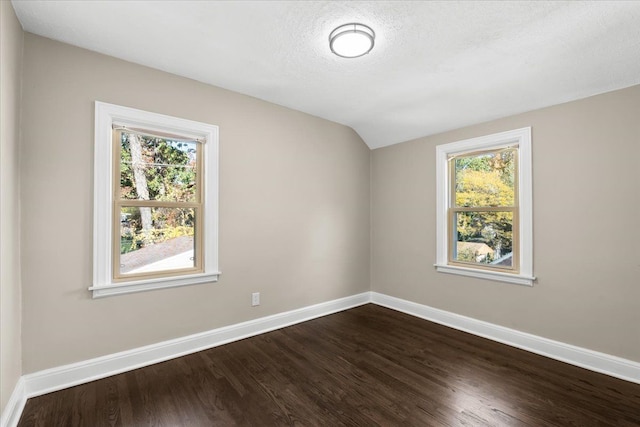 spare room with dark hardwood / wood-style floors, vaulted ceiling, and a textured ceiling