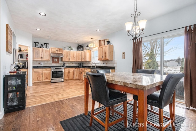 dining space with sink, an inviting chandelier, beverage cooler, and light hardwood / wood-style floors