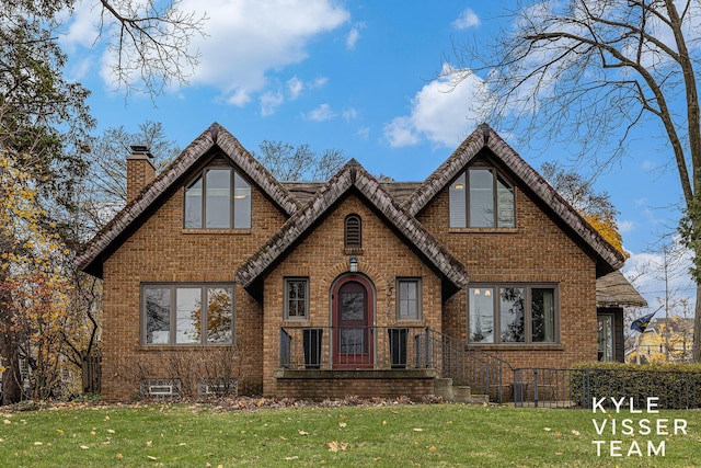 english style home with a front yard, brick siding, and a chimney