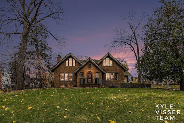 english style home featuring brick siding, a yard, and a chimney