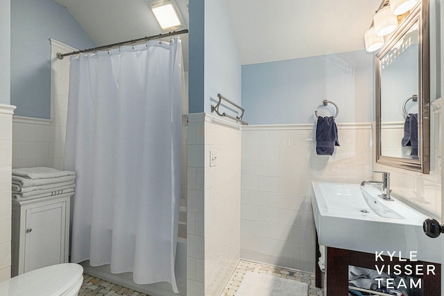 bathroom with a shower with shower curtain, toilet, a wainscoted wall, vanity, and tile walls