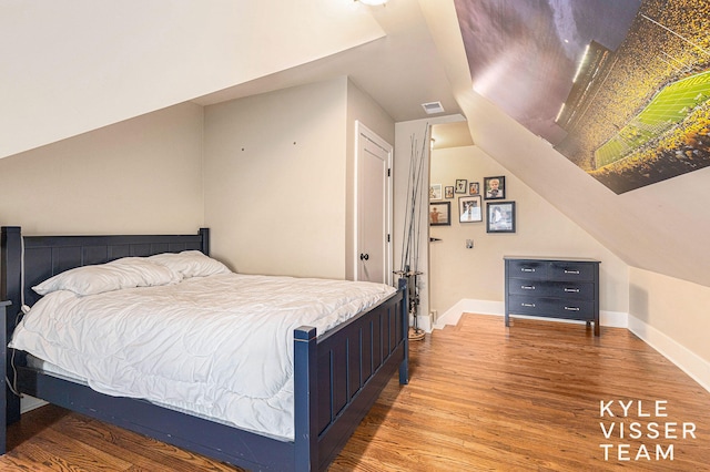 bedroom with lofted ceiling, visible vents, baseboards, and wood finished floors