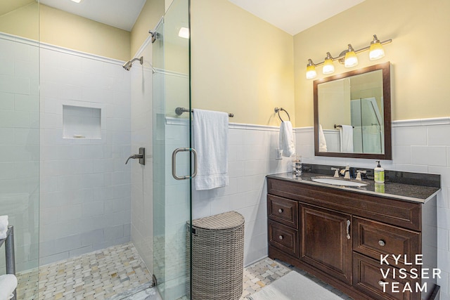 full bathroom with wainscoting, a tile shower, tile walls, and vanity