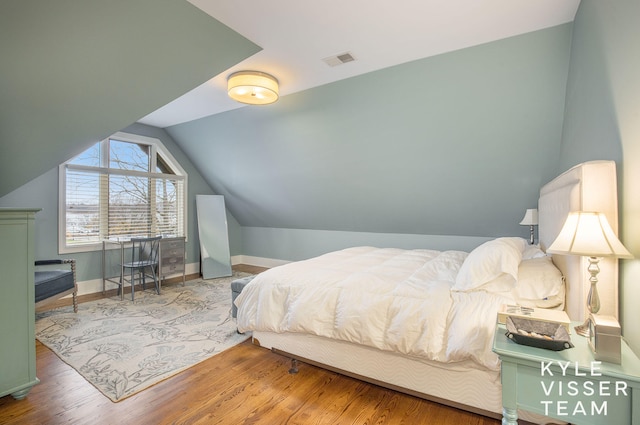 bedroom with vaulted ceiling, wood finished floors, visible vents, and baseboards