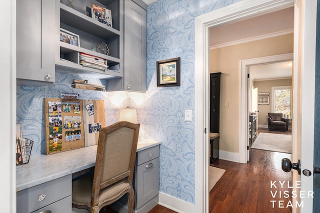 office space with baseboards, dark wood-style floors, wallpapered walls, built in desk, and crown molding