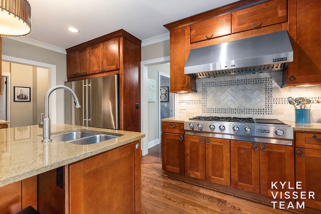 kitchen featuring crown molding, stainless steel appliances, a sink, wall chimney range hood, and light stone countertops