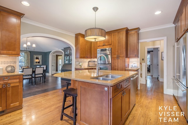 kitchen featuring stainless steel appliances, a sink, a center island with sink, and pendant lighting