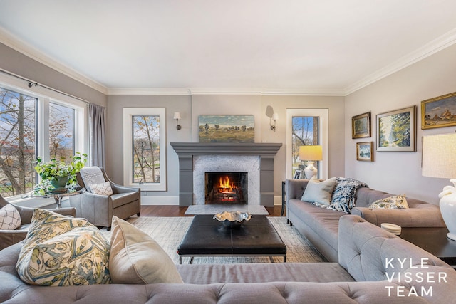 living room featuring a warm lit fireplace, crown molding, baseboards, and wood finished floors