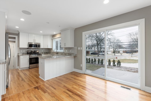 kitchen featuring sink, stainless steel appliances, light stone counters, white cabinets, and kitchen peninsula