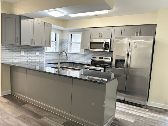 kitchen with appliances with stainless steel finishes, kitchen peninsula, sink, and dark stone countertops