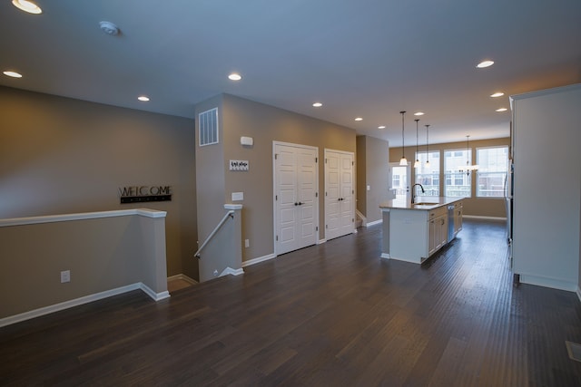 kitchen with sink, a center island with sink, stainless steel dishwasher, dark hardwood / wood-style floors, and pendant lighting